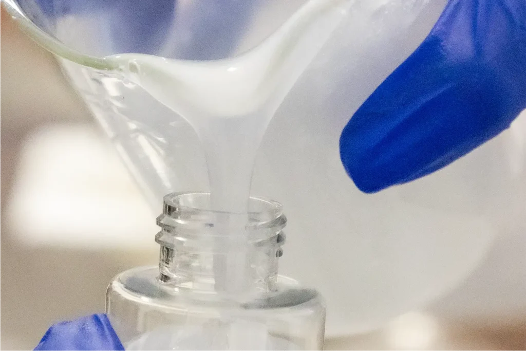 Close-up of laboratory technician pouring cosmetic formula into a small bottle