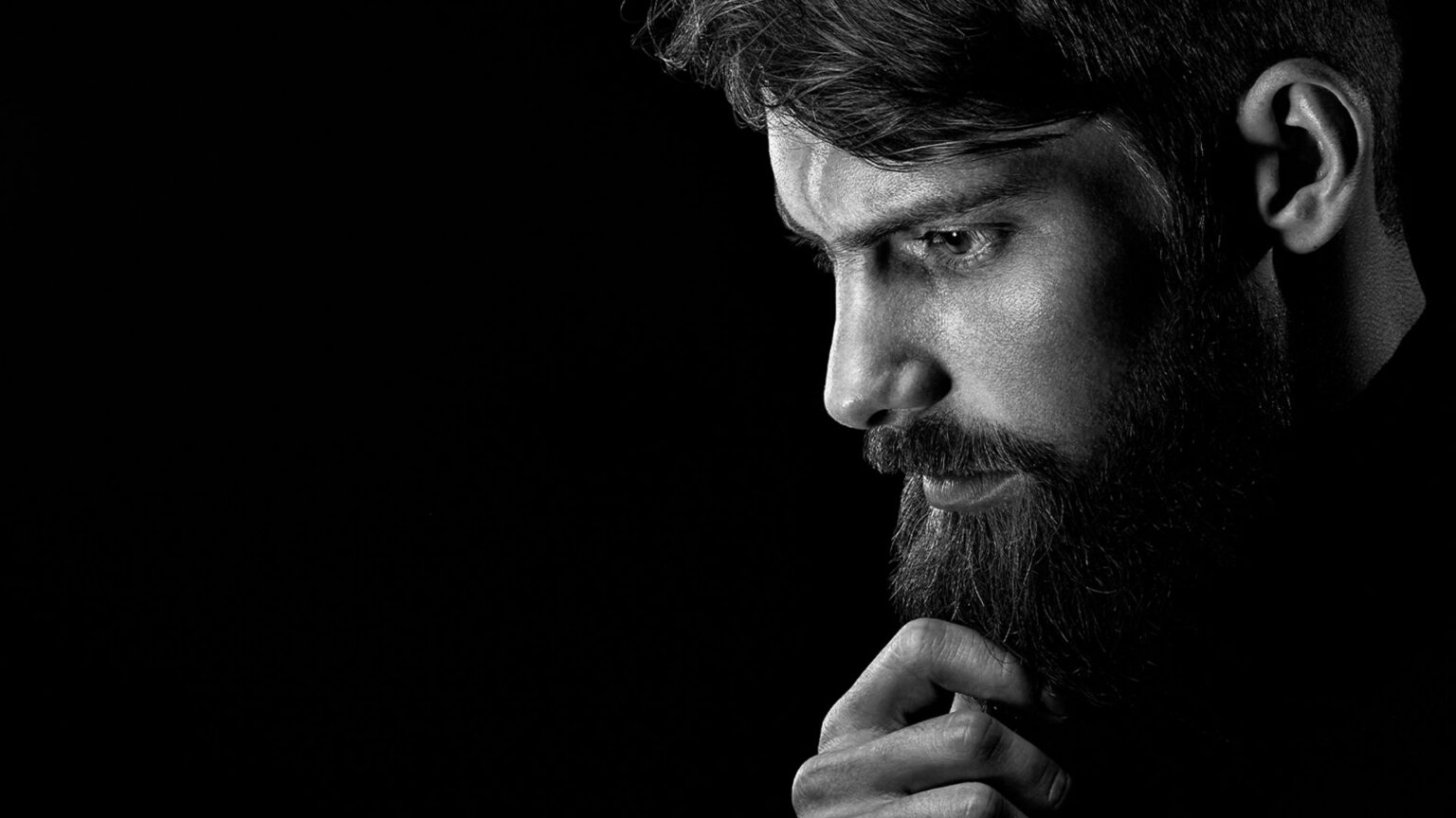 Close-up black and white portrait of a man with a beard in a thoughtful pose.