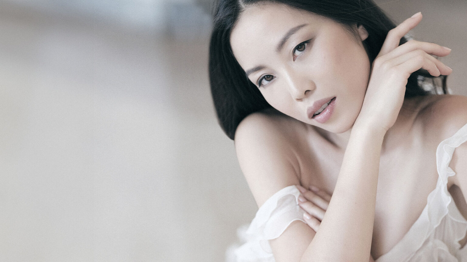 Portrait of a woman with smooth skin and soft natural makeup, photographed in a light and minimal studio setting.
