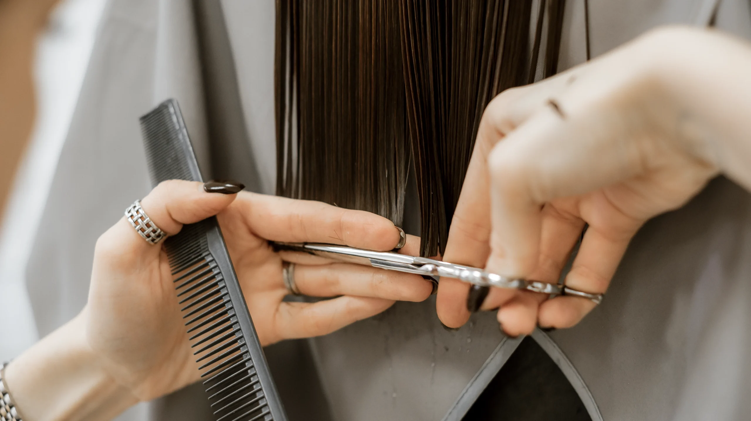 Close-up of a stylist performing an essential-level haircut, trimming straight hair with professional scissors and a comb for precision shaping