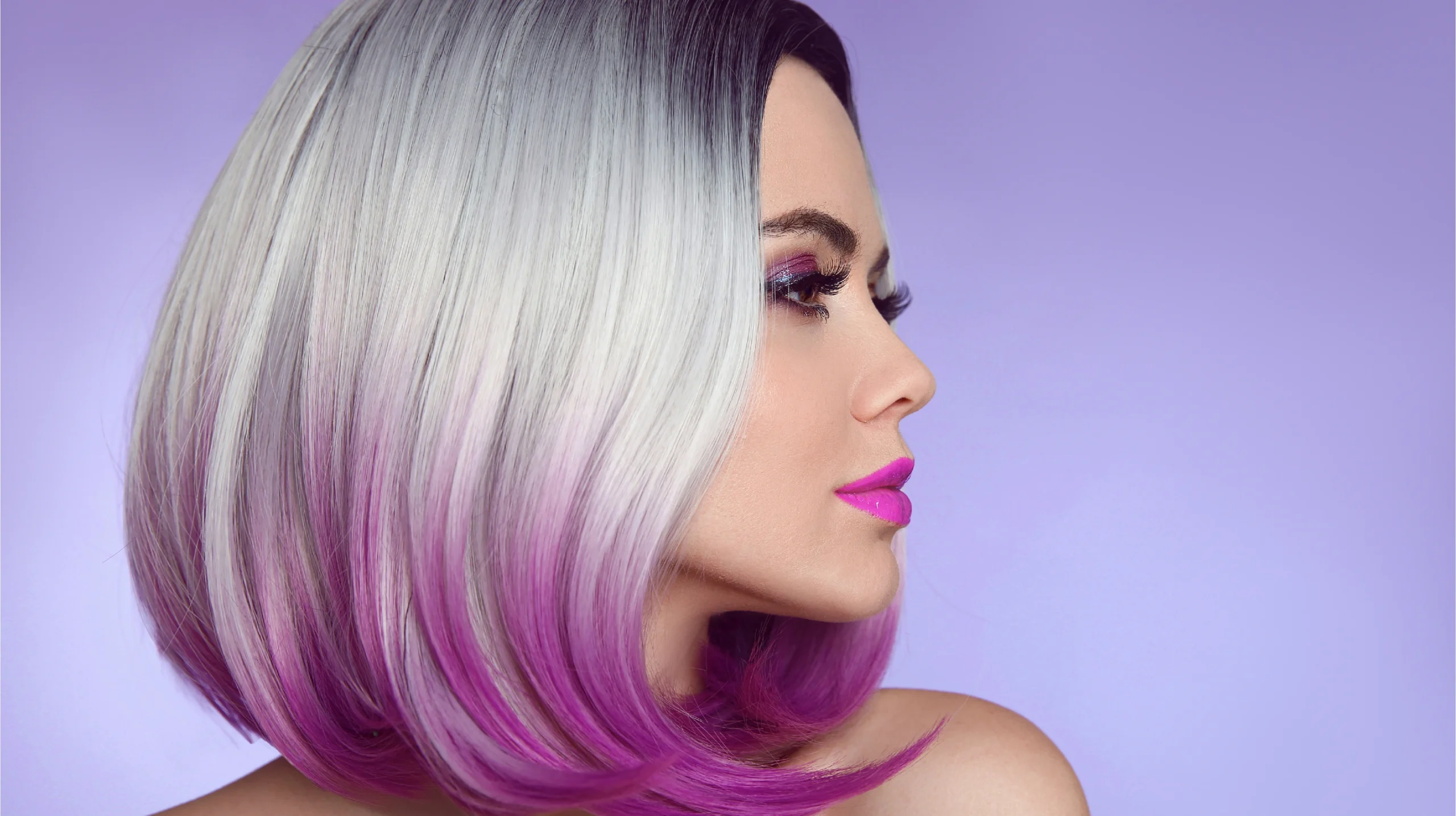 Profile view of a model with a smooth essential-level bob haircut, featuring clean lines and a rewind cutting technique enhanced by a silver-to-magenta color blend