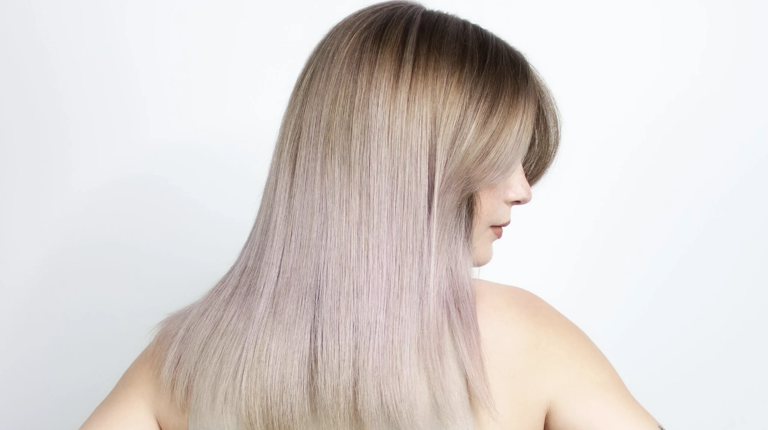 Side profile of a model with long, smooth hair featuring a soft gradient from natural blonde to subtle pastel tones on a clean white background
