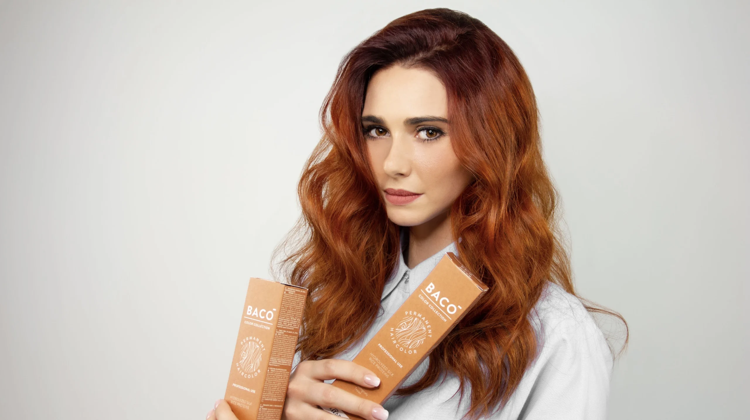 Model with copper-red hair holding Baco hair color boxes against a neutral background
